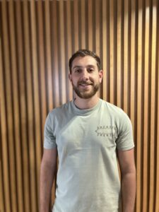 Portrait of Ashley Prema, operational co-ordinator of the Healthy and Sustainable Places Data Service - male stands in front of wooden backdrop