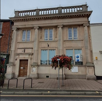 Shows large traditional bank building with boarded up windows. 