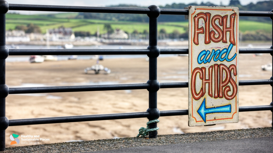 Fish and chips sign tied to railings with beach scene in background.